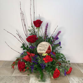 Red roses and purple flowers arranged around a memorial stone.