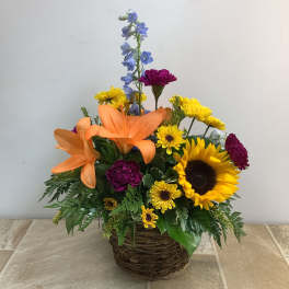 Mixed bouquet in a wicker basket with sunflowers, lilies, and blue delphinium