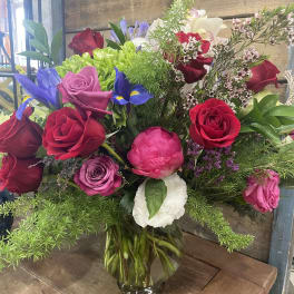 Mixed bouquet of roses, iris, and peonies in a clear glass vase
