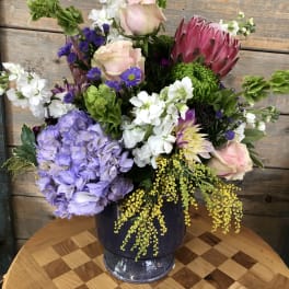 Mixed bouquet with pink roses, purple hydrangea, and a large pink protea in a vase
