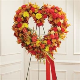 Heart-shaped floral wreath on a stand with red, orange, and yellow flowers.