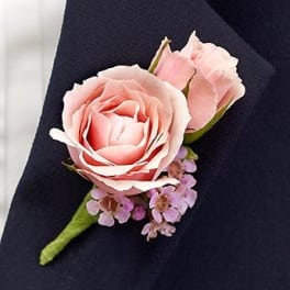 Pink rose boutonniere with small lavender filler flowers on dark fabric