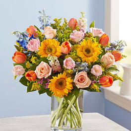 Colorful bouquet of tulips, roses, and sunflowers in a clear glass vase