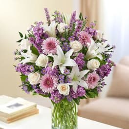 Bouquet of white lilies, pink daisies, and purple flowers in a glass vase