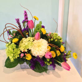 Mixed bouquet with pink tulips, hydrangeas, and yellow blooms in a low container