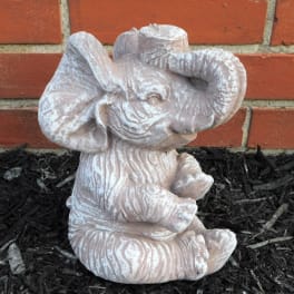 Small elephant figurine in a garden bed against a brick wall