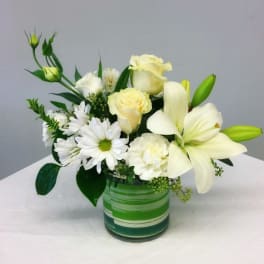 White lilies, roses, and daisies arranged in a green glass vase