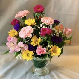 Mixed pink, yellow, and purple flowers arranged in a clear glass vase