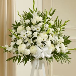 White funeral spray with lilies, daisies, and a satin ribbon on a stand