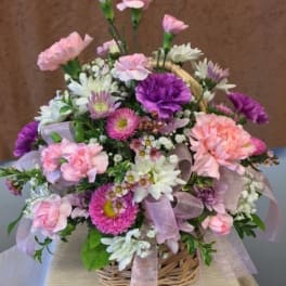 Basket arrangement of pink, purple, and white flowers with a ribbon