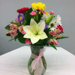 Mixed bouquet with a large white lily in a glass vase tied with pink ribbon