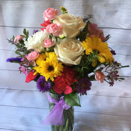 Mixed bouquet of roses, daisies, and carnations in a glass vase with a purple ribbon