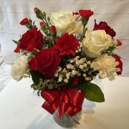 Red and white roses with carnations in a glass vase tied with a red ribbon