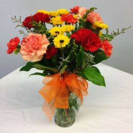 Bouquet of red, yellow, and peach carnations in a glass vase with an orange ribbon