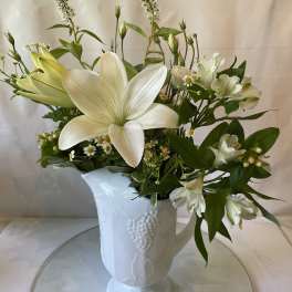 White lilies and small white flowers in a white ceramic vase