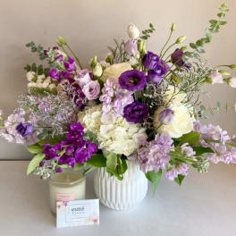 Purple and white bouquet in a white vase beside a candle