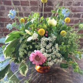 Mixed floral arrangement in a copper vase with blue, yellow, white, and pink blooms