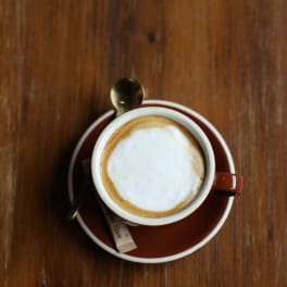 Cup of cappuccino on a saucer with a spoon on a wooden table