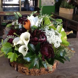 Mixed floral arrangement with white calla lilies and burgundy blooms in a wood base