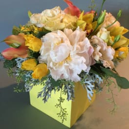 Yellow and white floral arrangement in a square box with pink calla lilies