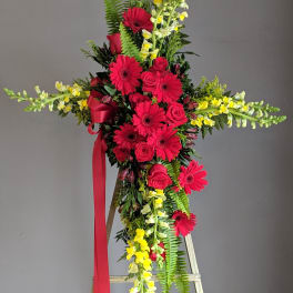 Standing floral cross with red roses, gerbera daisies, and yellow snapdragons