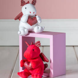 Two plush dragon toys holding glittery hearts on a pink block
