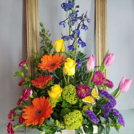 Colorful mixed flower arrangement in a wooden box with tall blue blooms