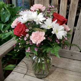 Mixed bouquet of red roses, white daisies, and pink carnations in a clear glass vase
