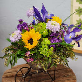 Mixed arrangement of sunflowers and purple irises in a small metal wheelbarrow container