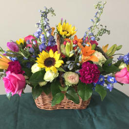 Colorful mixed flower basket with sunflowers, roses, lilies, and blue spikes