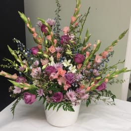 Mixed pink and purple floral arrangement in a white container