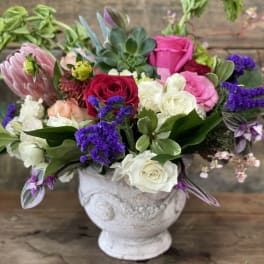 Mixed bouquet of roses and purple blooms in a white vase