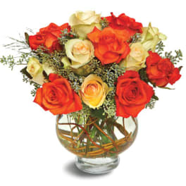 Round arrangement of orange and cream roses in a clear glass bowl vase