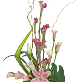 Tall arrangement of pink lilies and calla lilies with linear greenery in a cream urn vase.