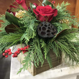 Red roses arranged with evergreen foliage and berries in a wooden box