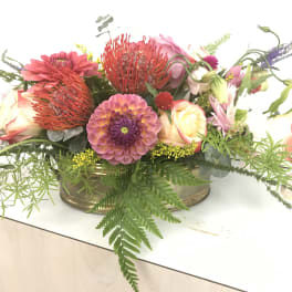 Low floral arrangement with pink, peach, and purple blooms in a shallow container