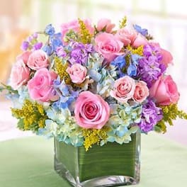 Pink roses and purple flowers arranged in a square glass vase
