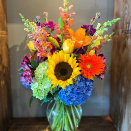 Bright mixed bouquet with sunflower, gerbera daisy, hydrangea, and snapdragons in a glass vase