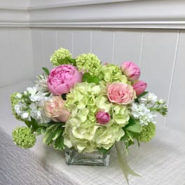 Pink peonies and roses arranged with green hydrangeas in a glass vase