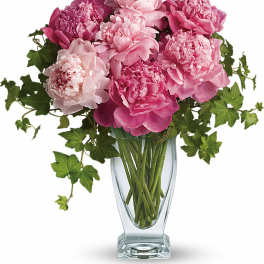 Pink peonies arranged in a clear glass vase with trailing ivy