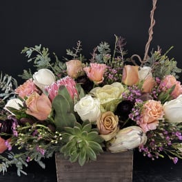 Low arrangement of peach and white roses with protea and succulents in a rustic wooden box