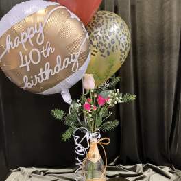 Birthday balloons with a small pink rose arrangement in a bottle vase