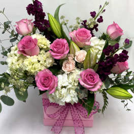 Pink and white flower arrangement in a pink box with a bow