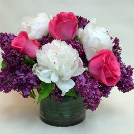 Pink roses and white peonies in a glass vase with purple lilacs