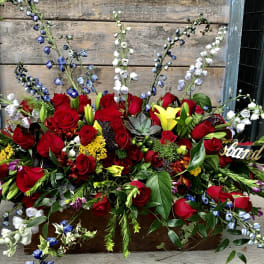 Large red rose arrangement with blue and white accent flowers in a wooden box
