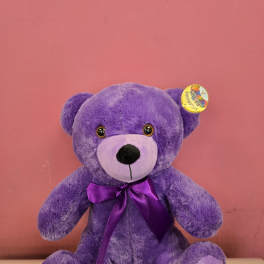 Purple teddy bear with a satin bow against a pink background