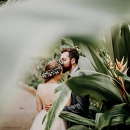 Bride and groom kissing among tropical plants with a floral crown