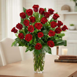 Tall arrangement of long-stem red roses in a clear glass vase on a table