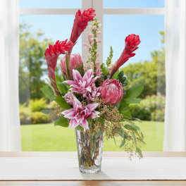 Tall pink lilies and protea with red tropical blooms in a clear glass vase