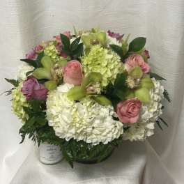 Low round bouquet of white hydrangeas, pink roses, green orchids in a glass vase with a candle beside it